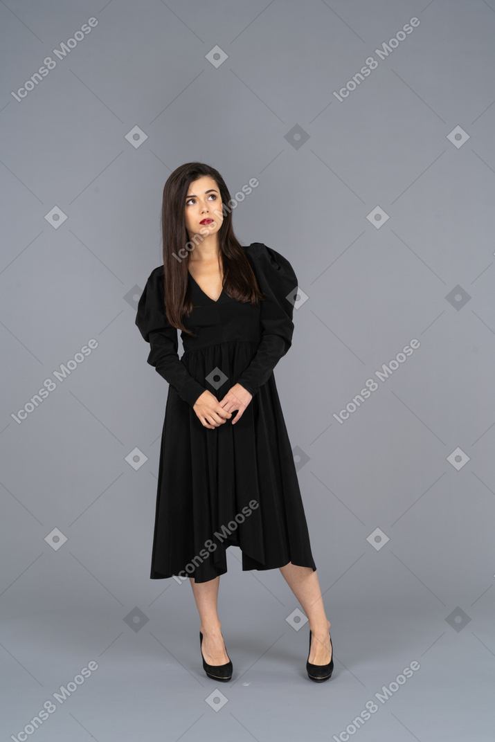 Vorderansicht einer jungen dame in einem schwarzen kleid, das hände zusammenhält