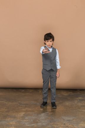 Вид спереди на симпатичного мальчика в сером костюме, стоящего с протянутой рукой