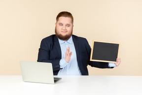 Ernster schauender junger überladener büroangestellter, der kleine tafel hält