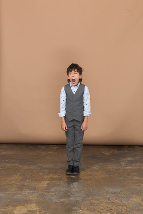 Vista frontal de un niño en traje mirando a la cámara y bostezando