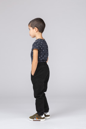 Vue latérale d'un garçon mignon dans des vêtements décontractés posant avec les mains dans les poches