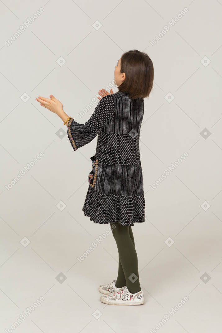 Vista posterior de tres cuartos de una niña sorprendida en vestido extendiendo los brazos