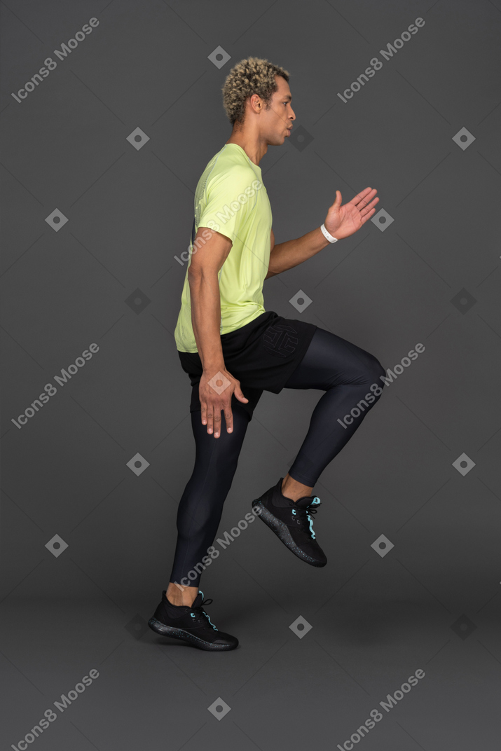 Side view of a jumping dark-skinned young man raising hand and bending knee