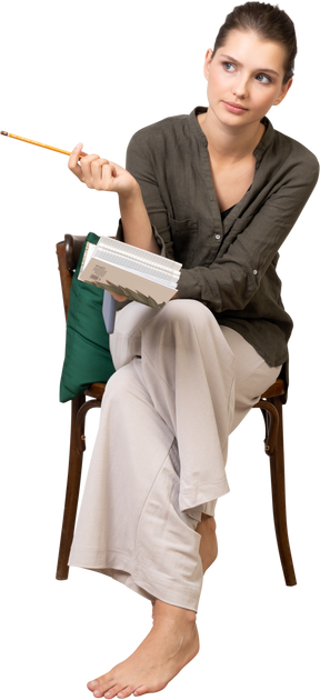 Front view of a thoughtful young woman wearing home clothes sitting on a chair with pencil and notebook
