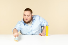 Young overweight househusband cleaning surface with spray