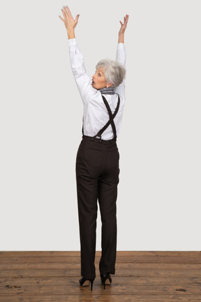 Three-quarter back view of an old lady in office clothing raising her hands