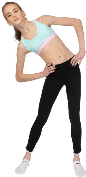 Vue de face d'une adolescente en tenue de sport mettant les mains sur les hanches en se penchant à gauche
