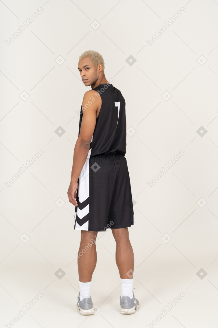 不審な若い男性のバスケットボール選手が頭を回してカメラを見ている背面図
