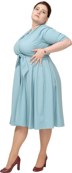 Вид спереди женщины в синем платье позирует с руками на бедрах