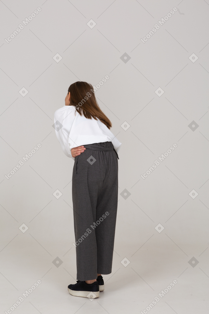 Vista traseira a três quartos de uma jovem senhora com roupas de escritório e dor de estômago, curvando-se