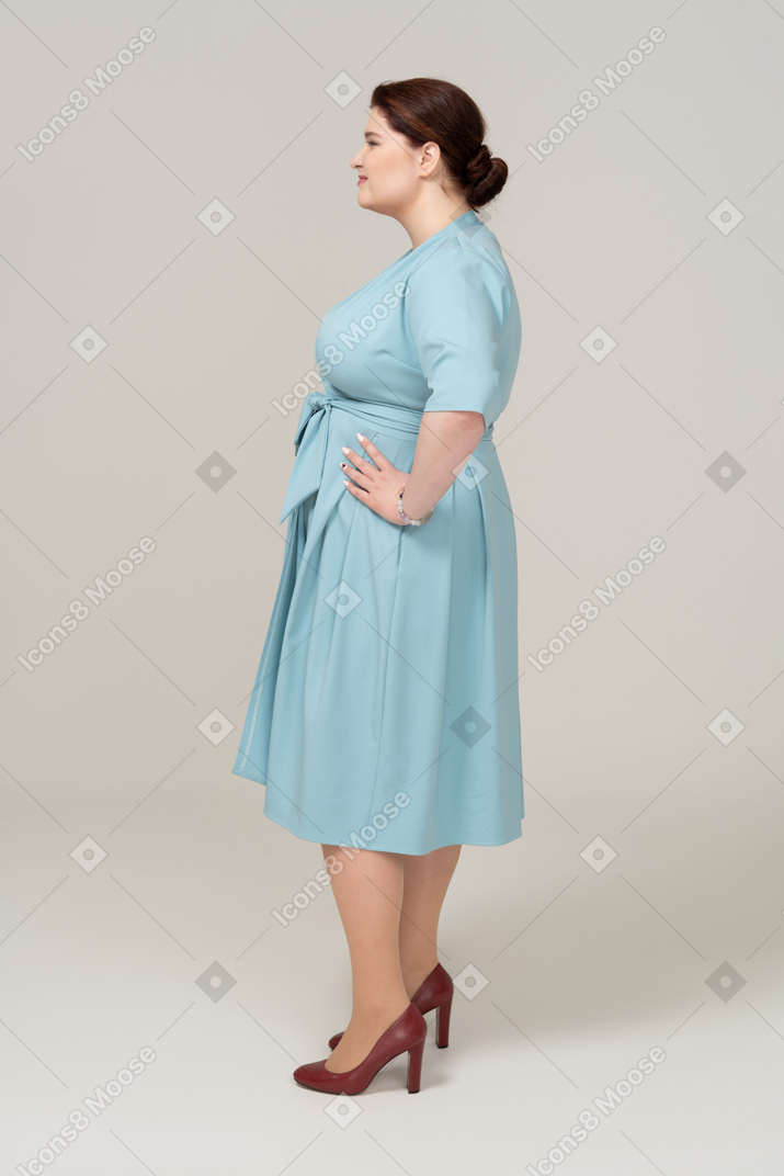 Vista lateral de uma mulher de vestido azul posando com as mãos na cintura