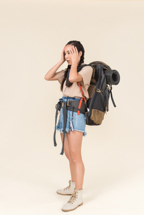 Worried female hiker with huge backpack touching head with both hands