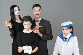 Miembros de la familia addams apuntando a un niño confundido en uniforme de marinero