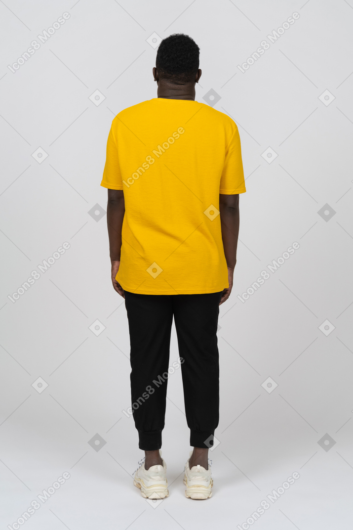 一个身穿黄色 t 恤的黑皮肤青年站在后面的背影