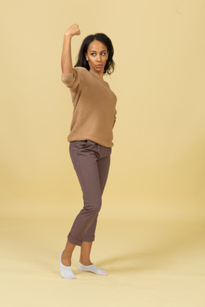 Side view of a strong dark-skinned young female raising hand while putting hand on hip