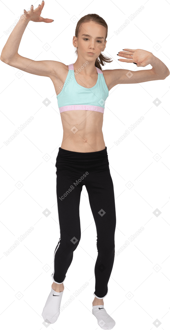 一个年轻的女孩，穿着运动服，跳舞时举起两只手的前视图