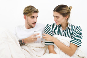 Pareja sentada en la cama y tomando café