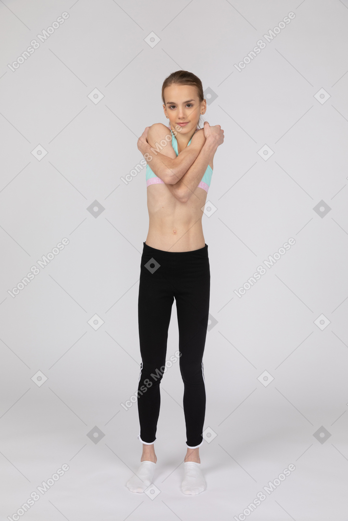 Front view of a teen girl in sportswear embracing herself