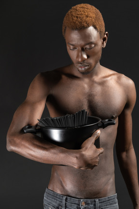 Close-up de um homem sério segurando uma panela preta com macarrão