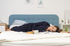 Front view of a laying in bed young lady having breakfast