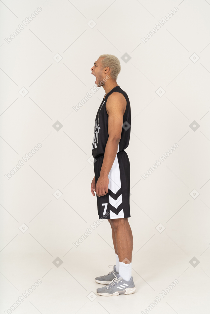 Vista lateral de un bostezo joven jugador de baloncesto de pie todavía