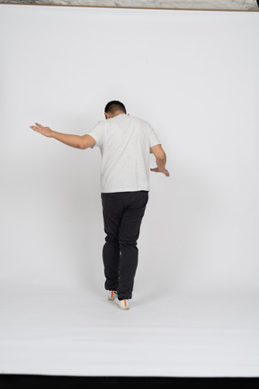 Vista traseira de um homem em roupas casuais andando com os braços estendidos