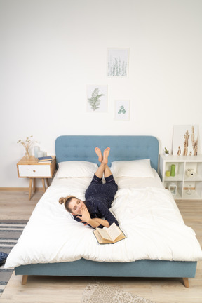 Vista frontal de uma jovem lendo livro feminino na cama