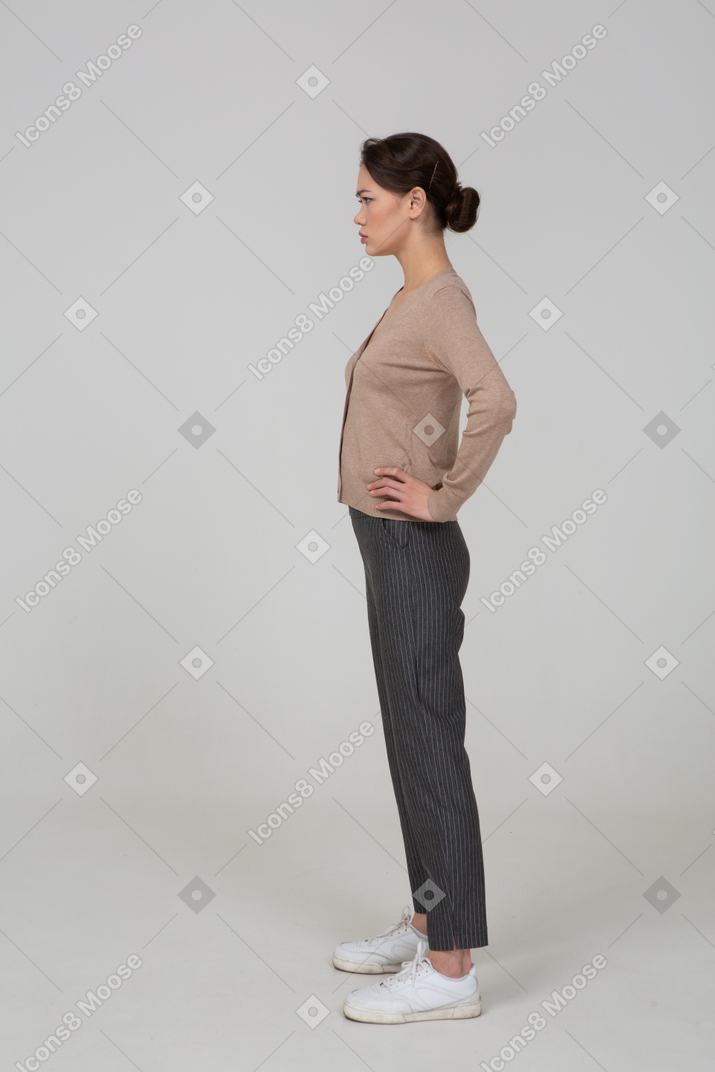 Side view of an angry young lady in pullover and pants putting hands on hips