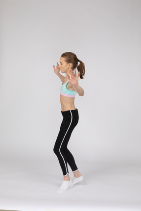Vista lateral de una jovencita en ropa deportiva de equilibrio de puntillas mientras levanta las manos
