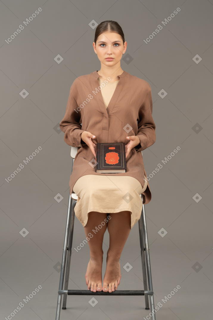 Jeune femme assise sur une chaise et montrant un livre
