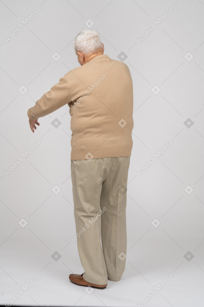 Rear view of an old man in casual clothes standing with extended arm