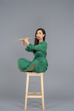 Figura intera di una giovane donna che suona il clarinetto seduta con le gambe incrociate su una sedia di legno