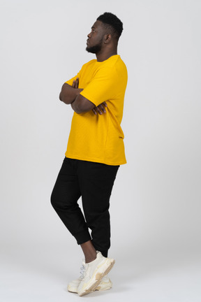 Vista de tres cuartos de un sospechoso joven de piel oscura con camiseta amarilla cruzando los brazos