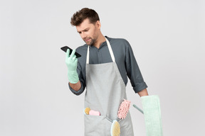 Young househusband holding mop and looking at phone