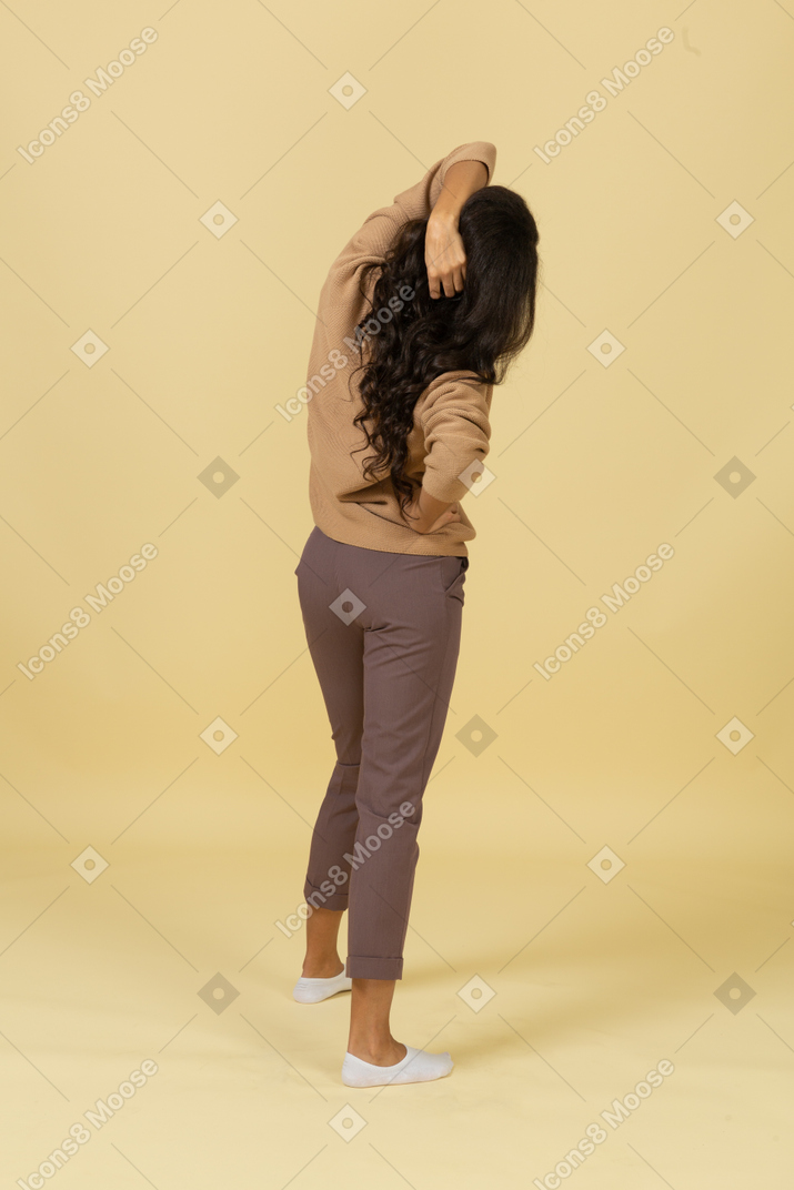 Vista posterior de tres cuartos de una mujer joven de piel oscura tocando el cabello