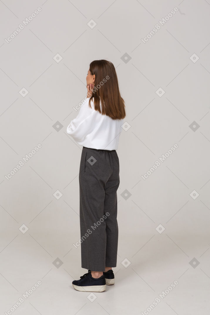 Three-quarter back view of a young lady in office clothing touching face
