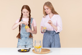 Two girls putting pieces of lemon into the water
