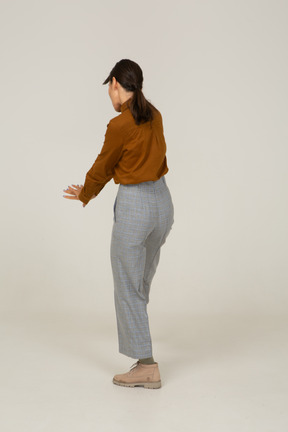Vista traseira a três quartos de uma jovem mulher asiática de calça e blusa estendendo as mãos
