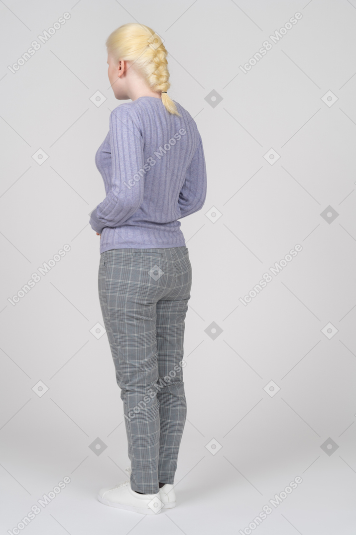 Three-quarter back view of a standing young woman looking away