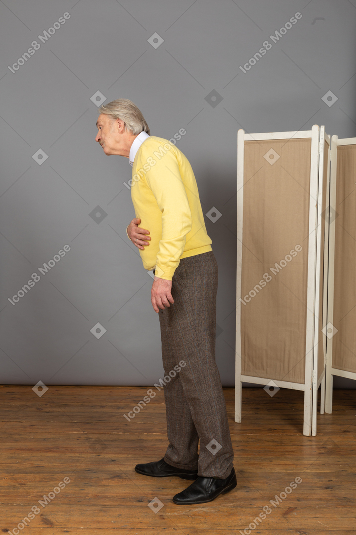 Side view of an old man putting hand on stomach while leaning forward