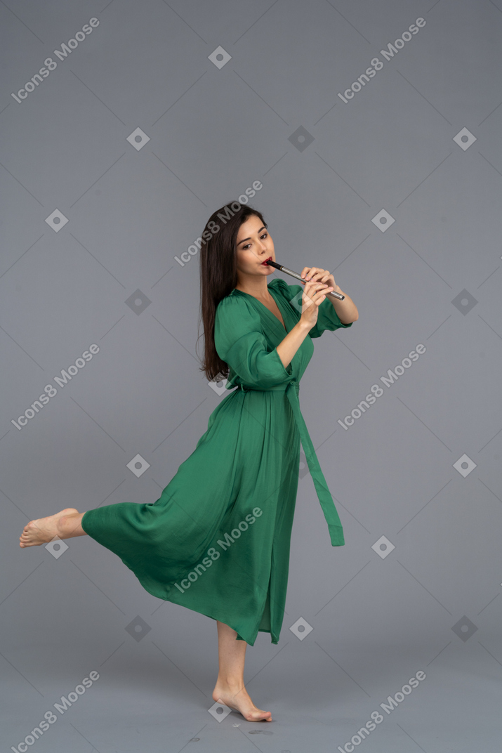 Side view of a barefooted young lady in green dress playing the flute
