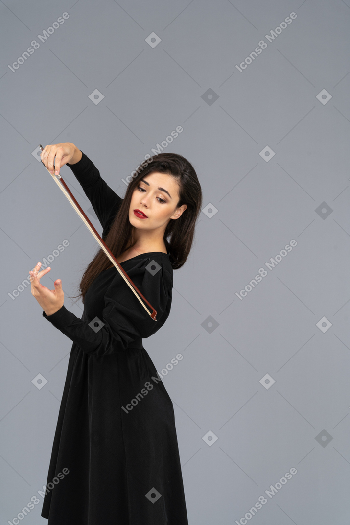 Vista di tre quarti di una giovane donna in abito nero che fa l'impressione di suonare il violino