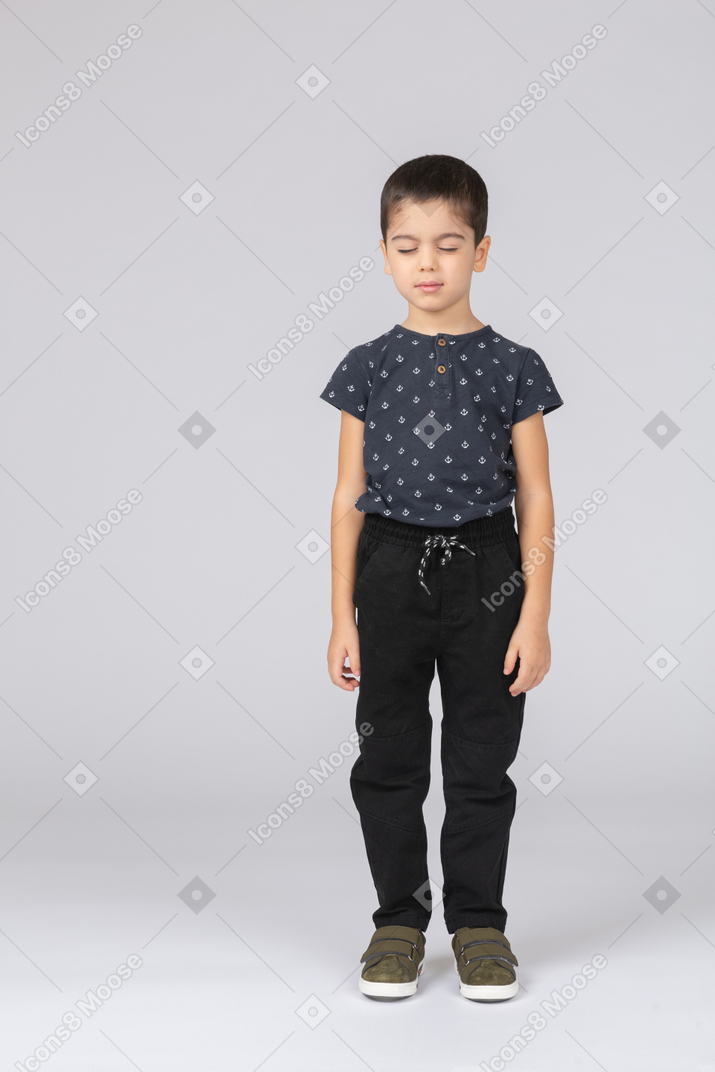 Front view of a cute boy in casual clothes standing with closed eyes