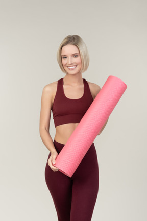 Smiling young woman in sportswear holding yoga mat