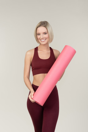 Souriante jeune femme en tenue de sport, tapis de yoga