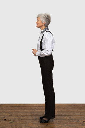 Vista laterale di una vecchia donna educata vestita in abiti da ufficio mettendo le mani insieme