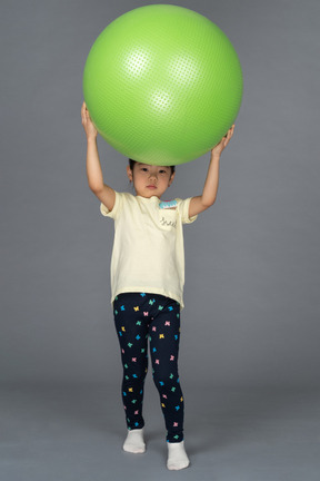 Niña sosteniendo un fitball verde sobre su cabeza