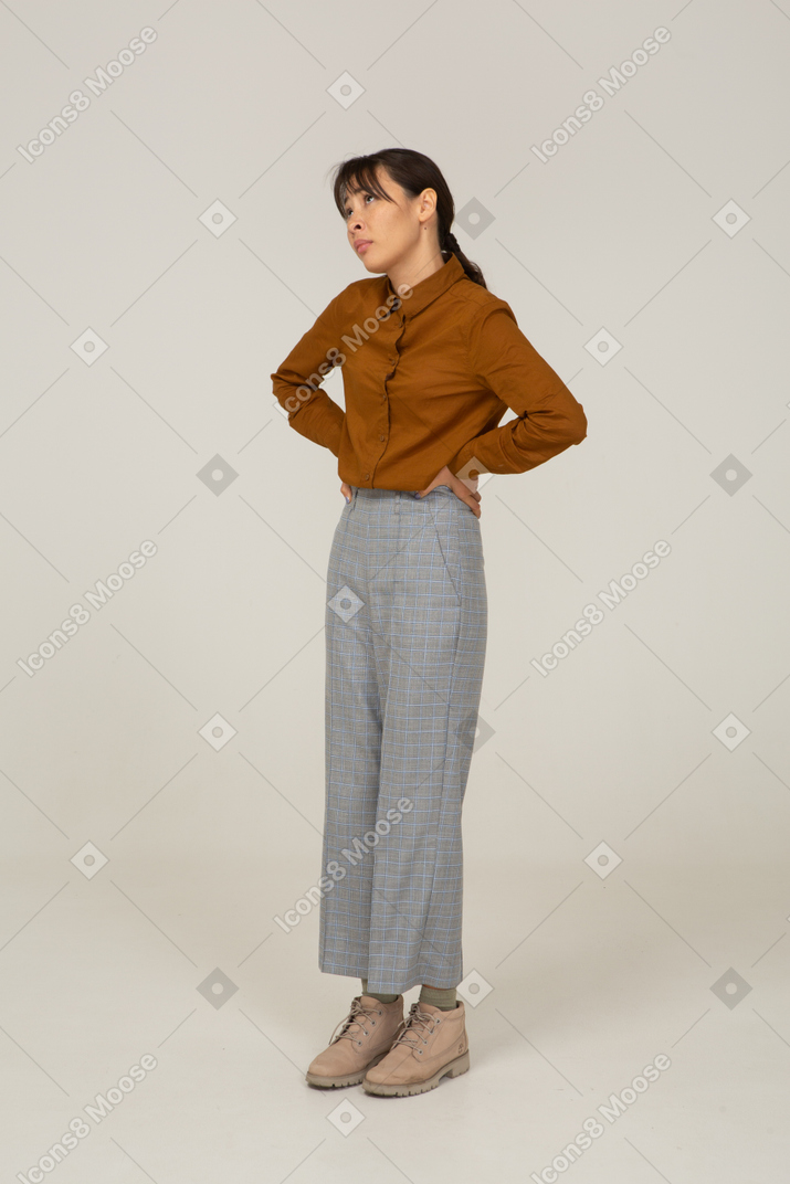 Vista de tres cuartos de una joven mujer asiática en calzones y blusa poniendo las manos en las caderas