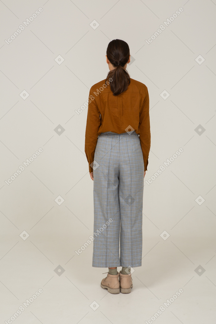 一位身着马裤和衬衫的年轻亚洲女性站着的后视图