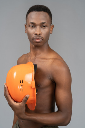 A shirtless young man holding a safety helmet